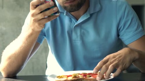 Bearded Man Eating Sandwich and Using Phone