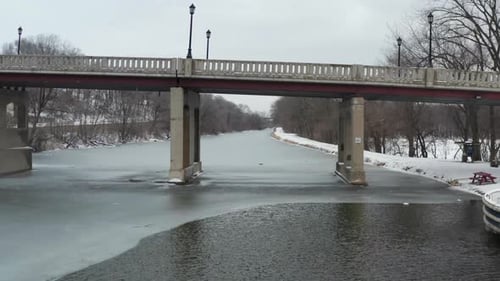 Flying under small bridge past touristic boat on frozen river