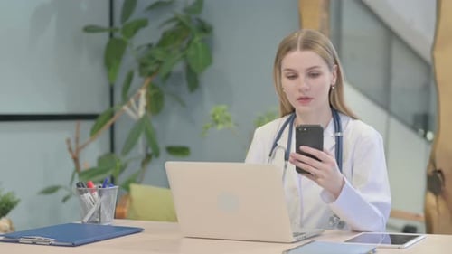 Young Woman Doctor Using Phone at Desk