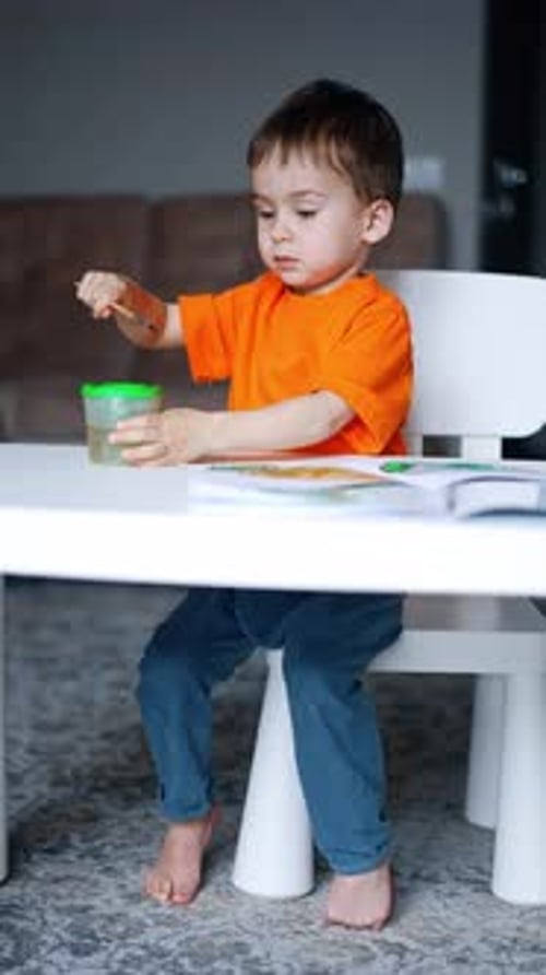 Three-year-old toddler sits at desk painting.