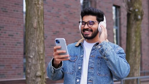 Smiling Laughing Handsome Young Indian Man in Glasses Listening Music on Street
