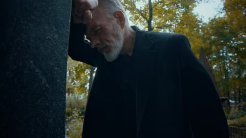 Man Grieving in a Cemetery Leaning on Tombstone