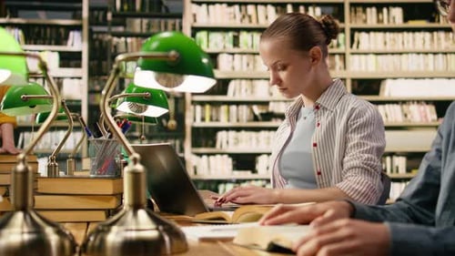 Jeune étudiante travaillant sur un ordinateur portable à la table en bois de la bibliothèque