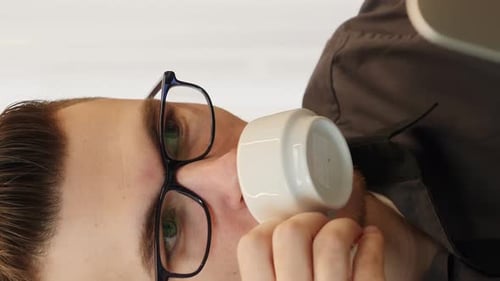 Porträt eines Mannes, der im Büro Kaffee trinkt und auf den Laptop-Bildschirm schaut. Vertikal