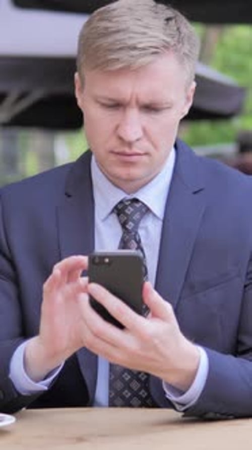 Businessman Using Smartphone while Sitting in Outdoor Cafe, Vertical Video