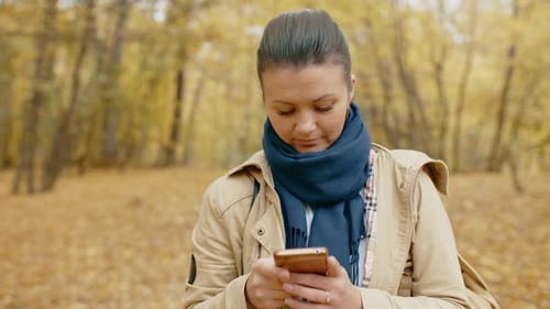Girl Communicates Through a Social Network on a Smartphone in an Autumn Park