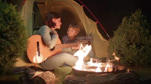 Woman and Child Play Guitar Near Tent at Night