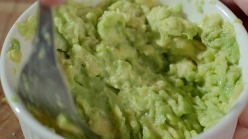 Mashing an Avocado with Fork in White Bowl