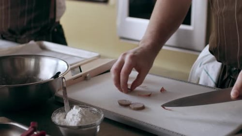 Chefs peel small onions on white cutting board in bright interior kitchen