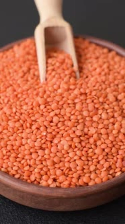Red Lentils Filling Wooden Bowl with Wooden Spoon