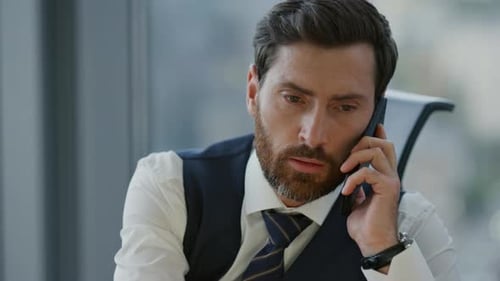Confident bearded businessman talking phone in modern office close up