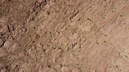 Aerial looks down onto barren rock landscape to desert sand in Bolivia