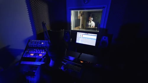 Music producer working in the little dark recording room. Sound engineer looks at computer screen.