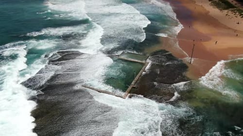 Aerial shot of waves and powerful ocean swell crashing over Monavale Rock Pool in Sydney, Australia