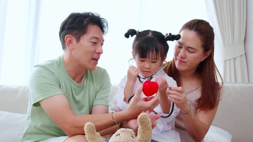 Happy family with daughter play doctor or nurse checkup and examining fever with heart shape.