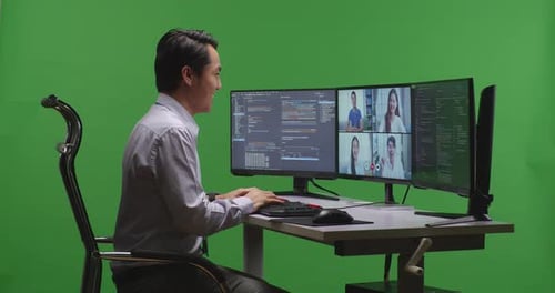 Asiatischer Entwickler, der Video hat, während er Code mit mehreren Computerbildschirmen auf grünem Bildschirm schreibt