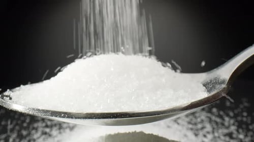 Pure white sugar cascades delicately into a spoon.