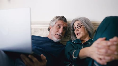 Senior Couple Relaxing in Bed Using Laptop
