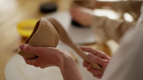 Artisan Molding a Clay Vessel with a Spatula on Potter's Wheel in Sunny Studio