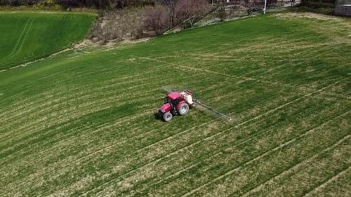 Aerial view of farming tractor spraying on field with sprayer, herbicides and pesticides insecticide