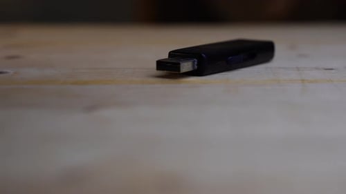 Black USB stick lies on a wooden board and rotates against a dark background