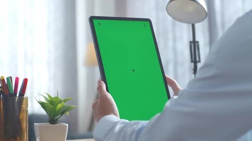Close up of man's hands holding a mock up green screen tablet on a desk