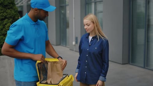 Cheerful Handsome African American Courier in Blue Uniform Delivering Food in Paper Packages to