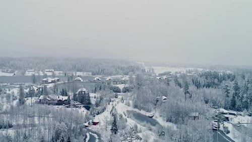 Aerial View Of Snow-covered Trees In The Forest, Cabin, And Frozen Lake During Winter.
