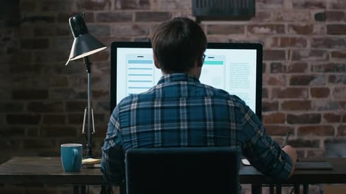 Young designer sitting in front of a monitor in a loft and sketching on a graphic tablet.