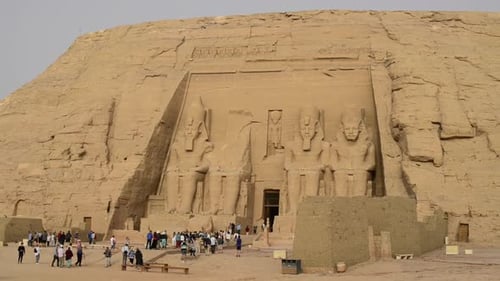 FRONT OF ABU SIMBEL TEMPLE, PHARAOH RAMSES II TEMPLE IN EGYPT WITH TOURISTS WALKING INSIDE WHILE A B