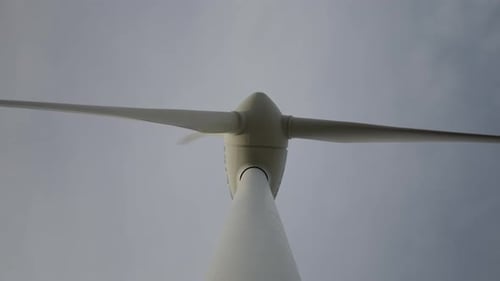 Low Angle Shot of Rotating Blades of a Wind Turbine with Cloudy Sky in the Background Slow Motion