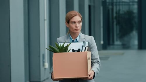 Woman With Light Skin Carrying a Box of Office Supplies Outside a Corporate Building