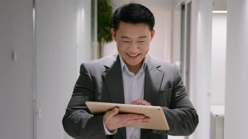 Smiling Man Uses Tablet in Office Hallway