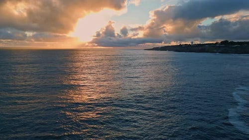 Golden sunlight reflects on dark ocean surface at sunrise in slow motion