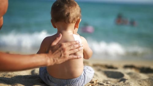 Nahaufnahme der jungen Mutterhand, die einen schützenden Sonnenschutz oder eine Sonnenschutzlotion auf ihr kleines Kind aufträgt