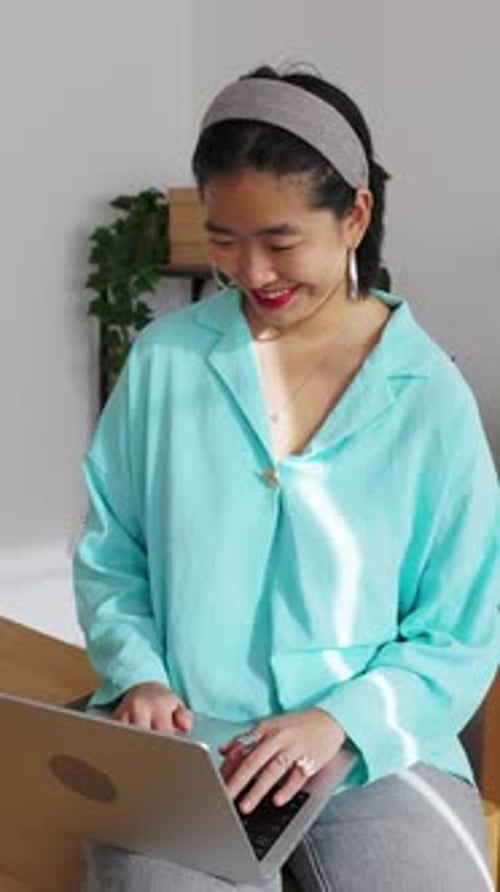 Smiling Asian Woman Working on Laptop in Minimalist Home Office
