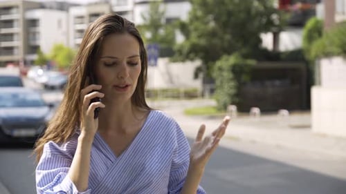 A Beautiful Young Caucasian Woman Talks Angrily on a Smartphone in a Street in an Urban Area