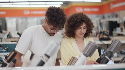 Young couple choosing hair dryer in electronics store in slow motion