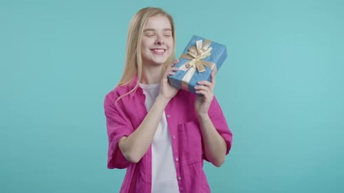 Happy Young Woman with Gift Box on Blue Studio Smiling Interested Whats Inside