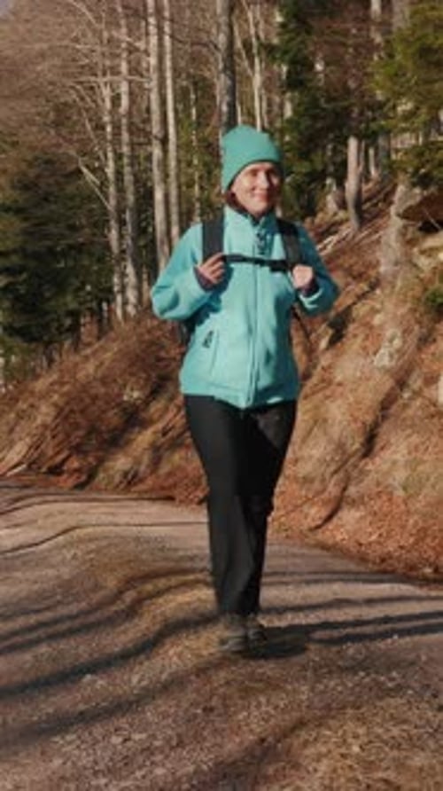 Female hiker in sportswear with backpack walking in fall forest. Vertical video