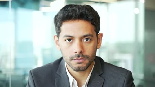 Close up. Portrait of a young serious successful businessman in a formal suit sitting at a workplace