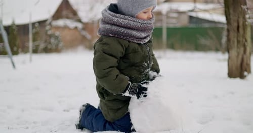 Child Building Snowball in Winter Garden