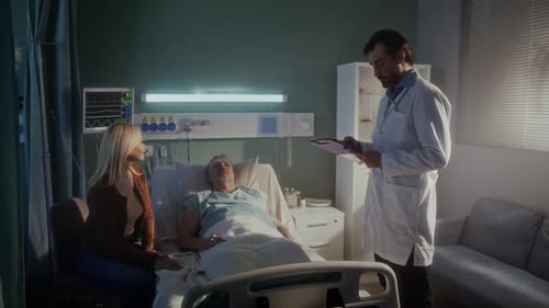 Doctor Consults Senior Couple About Disease By Hospital Bed