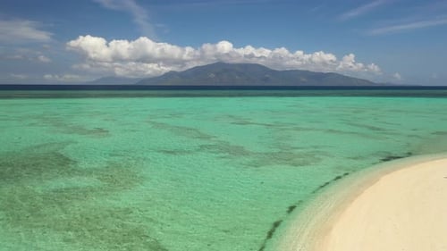 Young man standing alone on the beach, looking over the colorful and crystal clear water with fluffy