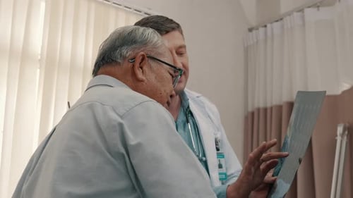 Male doctor explaining x-ray report to senior patient in medical practice.