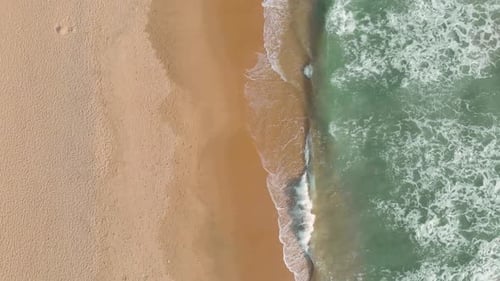 Aerial top down view of few tourists enjoying the landscape and sunny weather at the beach with wave