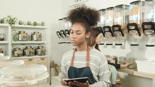 Two female shopkeepers work in zero waste and plastic-free grocery store.