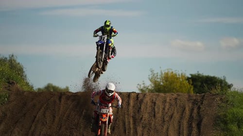 Skilled motocross riders on dirt track jumping over hill, moto competition, slow motion