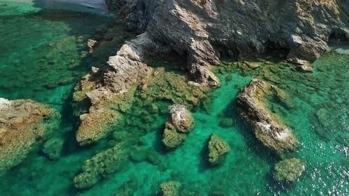 Clear blue water surrounding rocky coastal formations viewed from above on a sunny day