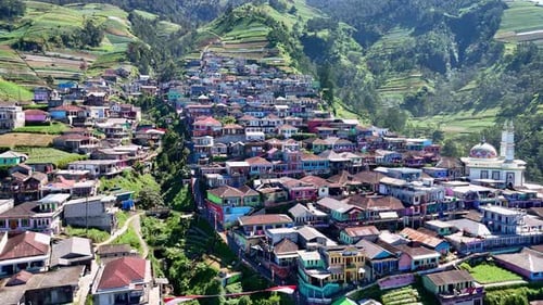 Aerial view of a village on a mountainside surrounded by greenery. The houses are built on terraces